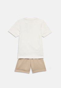 Λευκό βαμβακερό μπλουζάκι με κοντά μανίκια, σετάρισμένο με μπεζ βαμβακερά σορτς. Και τα δύο κομμάτια έχουν απλό, χωρίς στολίδια σχέδιο.