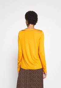 Langärmliges T-Shirt in leuchtendem Orange, mit Rundhalsausschnitt und lockerer Passform. Weicher, leichter Stoff mit glatter Textur.