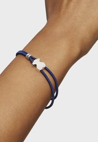 Bracciale in corda blu navy con un accento in argento a forma di animale stilizzato, caratterizzato da una superficie liscia e lucida e una chiusura sicura.