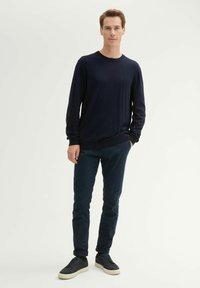 Granatowy sweter dzianinowy, okrągły dekolt, długie rękawy, połączony z ciemnoniebieskimi, slim fit spodniami i czarnymi trampkami z białą podeszwą. Prosty i nowoczesny design.