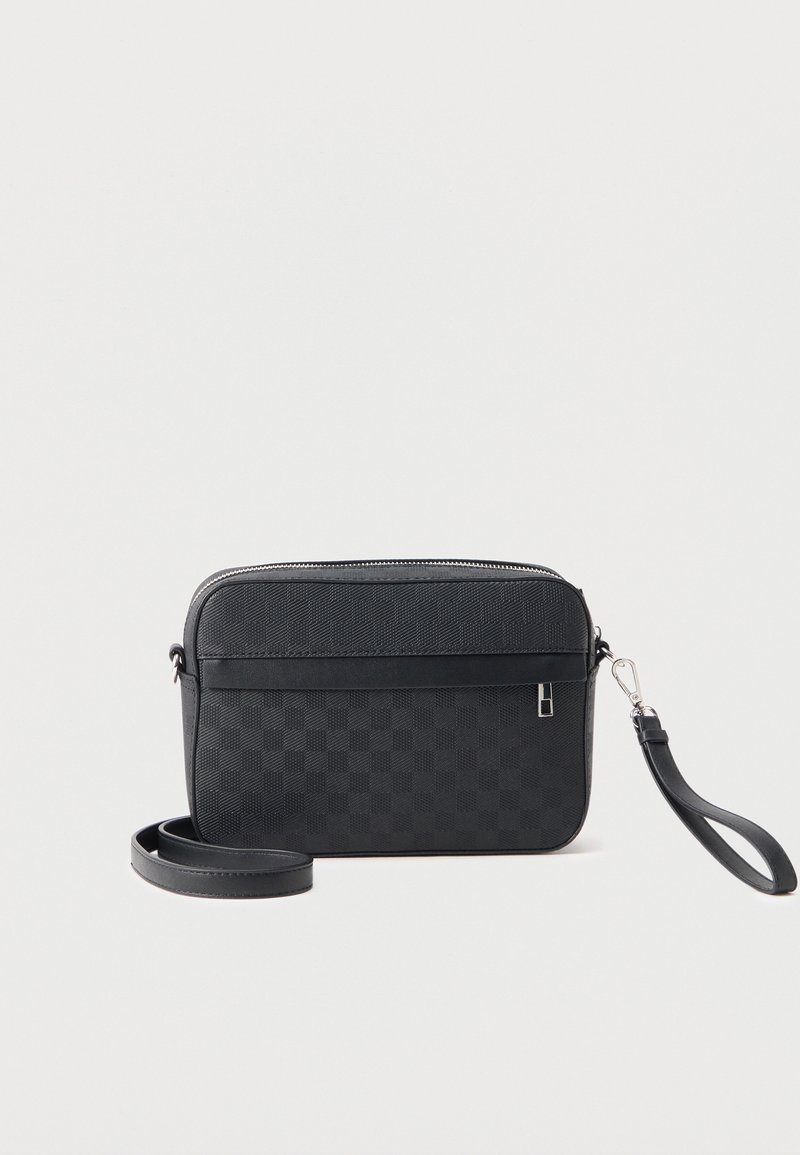 Μαύρη τσάντα χιαστί με υφή, επάνω μέρος με φερμουάρ, αποσπώμενο λουράκι καρπού και μακρύ ρυθμιζόμενο λουράκι ώμου σε λευκό φόντο.