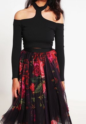 Kobieta ubrana w czarną prążkowaną bluzkę z odkrytymi ramionami i wysokim stanem, czarną spódnicę tiulową w kwiaty w kolorach czerwonym i różowym.
