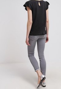 Czarna bluzka z krótkimi falbankowymi rękawami i kluczykiem na plecach, w połączeniu z dopasowanymi szarymi dżinsami i srebrnymi balerinami. Prosty design, luźny krój.