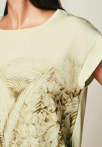 Lys grøn kortærmet top med et botanisk print i jordfarver. Glat stof med en afslappet pasform og rund udskæring.