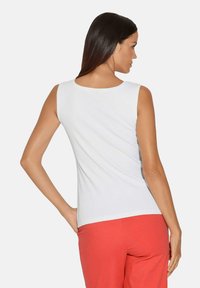 Witte geribbelde mouwloze top met een ronde hals, gecombineerd met koraalkleurige broek. De stof lijkt glad en aansluitend.