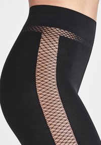 Svarta leggings med en slät yta och ett genomskinligt nätpanel samt ett geometriskt mönster i nude-färg längs utsidan av låret.