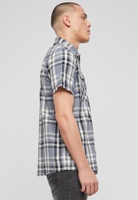 Kockovaná košeľa s krátkym rukávom v odtieňoch sivej a bielej, s golierom na gombíky a náprsným vreckom, vyrobená z ľahkej tkaniny.