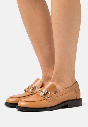 Mocassins en cuir marron clair avec un détail de chaîne dorée sur le dessus, dotés d'un bout arrondi et d'un petit talon bloc noir.