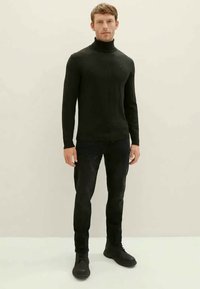 Pull à col roulé noir au design ajusté, avec une texture côtelée et des manches longues, associé à un jean noir et des bottines noires.