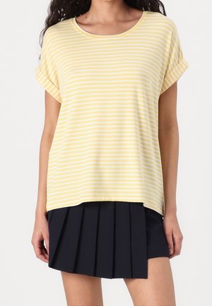 Vrouw draagt een geel-wit gestreept T-shirt met korte mouwen, gecombineerd met een zwarte geplooide minirok tegen een effen achtergrond.