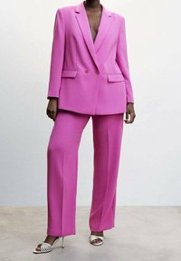 Fuksjowy garnitur składający się z dwurzędowej marynarki z wyłogami, prostych spodni oraz białych sandałów na wysokim obcasie z paskami.