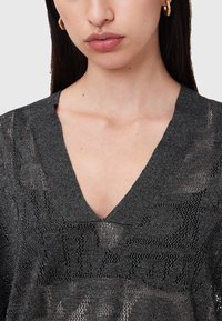 Schwarzes Strickoberteil mit V-Ausschnitt, das ein aufwendiges offenes Maschenmuster und eine weiche Textur aufweist. Akzente mit einem subtilen Glanz.