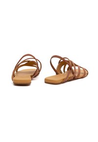 Braune Leder-Sandalen mit dünnen, gekreuzten Riemen und einer flachen, beigefarbenen Sohle. Das Design ist offen, minimalistisch und hat eine glatte Oberfläche.