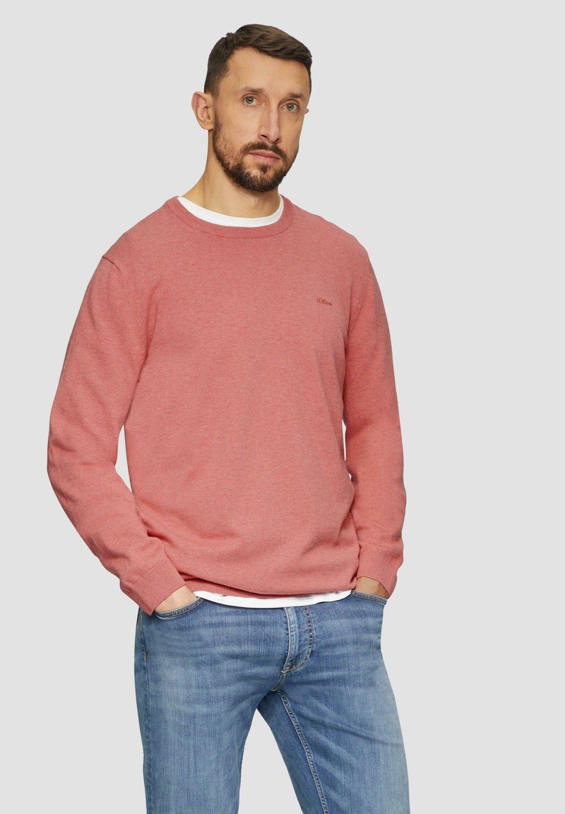 Roze gebreide trui met een ronde hals, lange mouwen en een subtiel logo detail. Gepaard met lichtblauwe denim jeans.