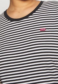 Sort-hvid stribet t-shirt med rund halsudskæring og et rødt Levi's logo-patch på venstre side. Blødt bomuldsstof.