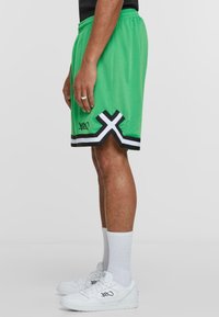 Groene mesh basketbalshorts met zwarte en witte accenten, met een kruispatroon aan de zoom en een logo-detail aan de zijkant.