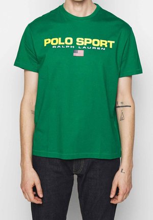 Grünes Baumwoll-T-Shirt mit gelbem Schriftzug "POLO SPORT" sowie darunter "RALPH LAUREN" und einer kleinen amerikanischen Flagge. Kurze Ärmel und Rundhalsausschnitt.