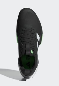 Baskets noires de sport avec tige texturée, rayures blanches, accents verts au talon et lacets plats. Comprend une languette rembourrée et une semelle en caoutchouc durable.