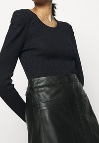 Schwarzes, geripptes Langarmoberteil mit rundem Ausschnitt, kombiniert mit einem schwarzen Lederrock mit glatter Textur und Fronttaschen.