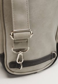 Szara torba z sztucznej skóry z czarnym dnem, z szerokim paskiem i błyszczącymi srebrnymi akcesoriami, w tym klipsem i pierścieniami do mocowania.