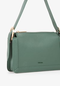 Borsa a tracolla in pelle verde con una finitura testurizzata, caratterizzata da una chiusura con zip, dettagli in oro e una tracolla regolabile. Forma rettangolare.
