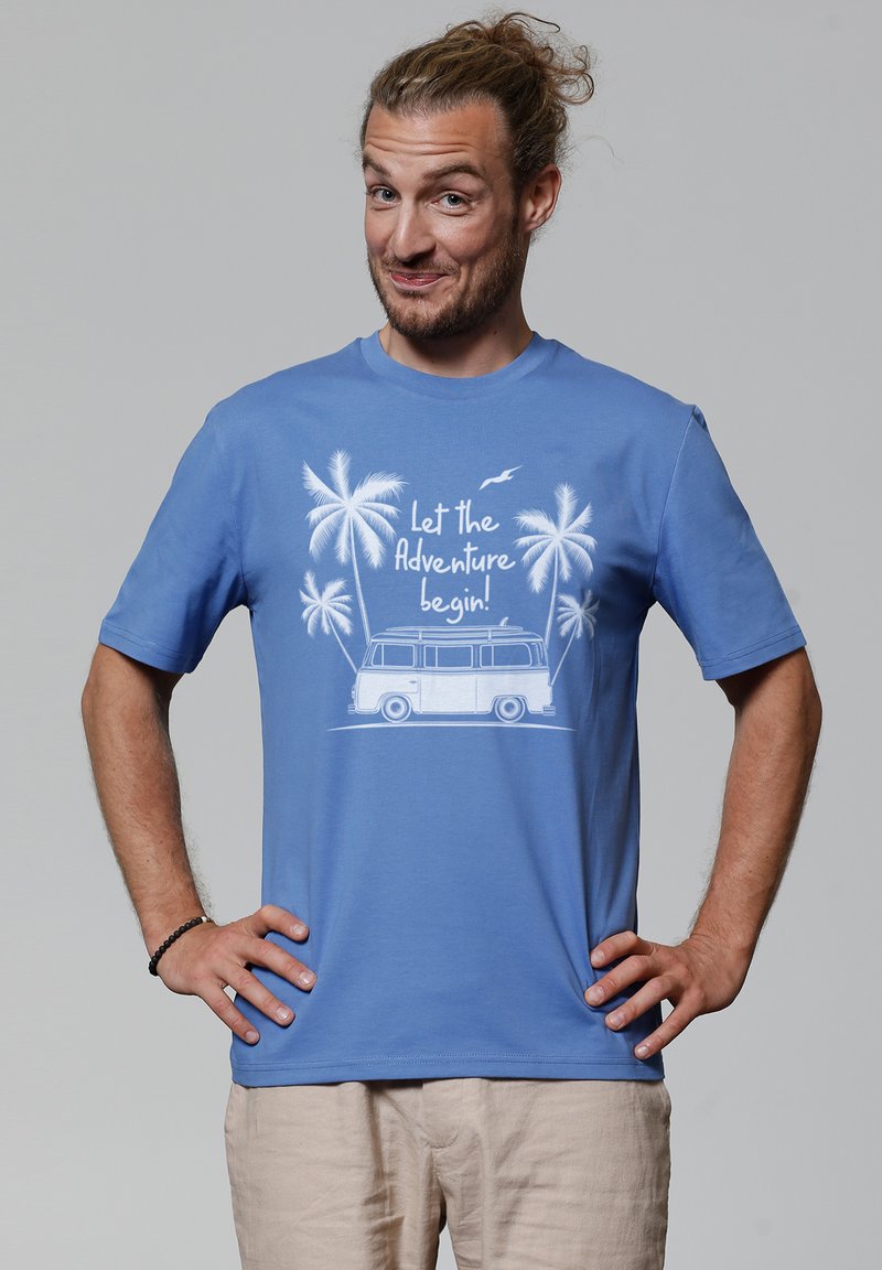 Blauwe katoenen t-shirt met een witte afbeelding van een vintage bus, palmbomen en de tekst "Laat het avontuur beginnen!" gedrukt op de voorkant.
