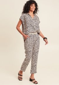 Twee-delig leopardprint outfit gemaakt van lichtgewicht stof; kortom shirt met kraag en taps toelopende broek; gecombineerd met zwarte blokhak sandalen.