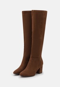 Botas de ante marrón hasta la rodilla con tacón ancho, que presentan una textura suave, puntera afilada y costuras visibles a lo largo de las costuras.