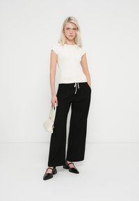 Haut en maille côtelée blanche à manches courtes, associé à un pantalon noir à jambes larges. Des ballerines noires et un petit sac à main blanc complètent la tenue.