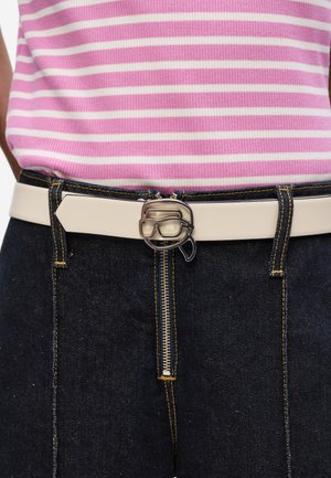 Weißer Gürtel mit einer metallischen Schnalle in Form einer Brille, kombiniert mit dunkelblauer Jeans. Das Oberteil hat pinke und weiße horizontale Streifen.