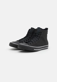 Vysoké černé plátěné tenisky s gumovým špičkovým krytem, vyznačující se černými tkaničkami, bílými pruhy na střední podrážce a texturovaným svrchním materiálem.