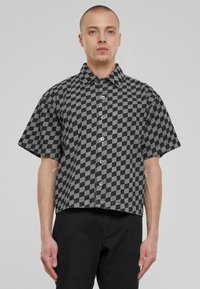 Camisa de cuadros de manga corta en tela negra y gris con un cierre de botones en la parte delantera, cuello amplio y corte holgado.