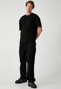 Sort bomulds-T-shirt med korte ærmer og rå kanter, parret med sorte cargo bukser med sidelommer og en afslappet pasform. Sorte sneakers.