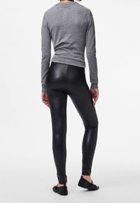 Black synthetic leggings with a shiny finish, paired with a fitted gray long-sleeve top. View from the back, showing form-fitting design.