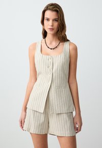 Beige linnen vest met verticale zwarte strepen, vierkante halslijn, vijf knopen, en twee voorzakken, gecombineerd met bijpassende shorts.