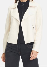Light cream faux suede jacket with a notched collar, zippered side pockets, and a fitted design, paired with a ribbed black turtleneck.