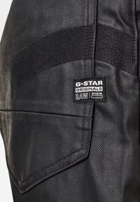 Černá denimová tkanina s texturovaným povrchem. Obsahuje značku G-Star a kapsu s diagonálním švem.