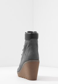 Stivaletto alla caviglia in suede grigio con collo imbottito nero spesso, tacco a cuneo e suola in gomma marrone testurizzata; presenta un design con lacci e dettagli con logo.