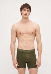 Boxeri din bumbac verde cu o croială ajustată, prevăzu�ți cu un tiv cu logo. Materialul pare moale și neted, cu un design minimalist, de lungime scurtă.