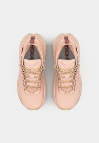 Des chaussures de sport rose clair avec une tige texturée, une semelle extérieure beige et des lacets élastiques. Comprend une languette rembourrée et un logo sur la semelle intérieure.