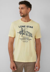 Lichtgele t-shirt met korte mouwen met de opdruk "LONE STAR MOTEL" in donkerblauw, met een ontwerp van een vintage motelbord. Zachte stoffen textuur.