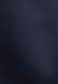 Tessuto blu navy con una superficie liscia, caratterizzato da motivi a coste diagonali. La superficie è uniforme, senza segni o decorazioni visibili.