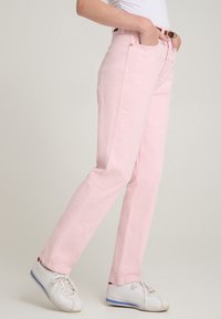Pantaloni in denim rosa con taglio dritto, tasche anteriori e cintura. Abbinati a sneaker bianche, mostrando un outfit casual.