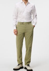 Ljusgröna chinos med slim fit, knappstängning och sidofickor, kombinerat med en vit långärmad skjorta och beiga skor.