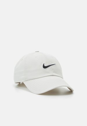 Weiße Nike-Baseballkappe mit schwarzem Swoosh-Logo, gebogenem Schirm und verstellbarem Riemen vor weißem Hintergrund.