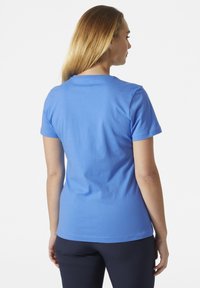 Camiseta de algodón azul con mangas cortas, cuello redondo y una textura suave. La vista trasera muestra un diseño sencillo sin logotipos ni patrones visibles.