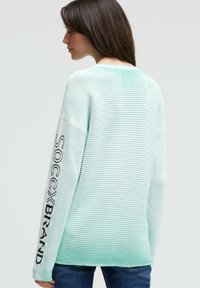 Hellmintgrüner, übergroßer Pullover mit geripptem Muster, der entlang des Ärmels den Schriftzug "SOCCX BRAND" in Schwarz trägt, mit rundem Ausschnitt und überschnittenen Schultern.