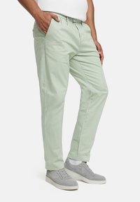 Light green cotton pants with a straight-leg design, featuring side pockets and a smooth texture, paired with grey low-top sneakers.