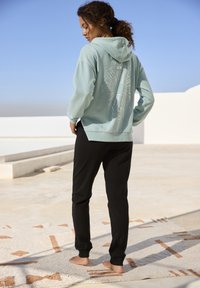 Hellblauer Hoodie mit einem Sonnenmotiv auf dem Rücken, kombiniert mit schwarzen Jogginghosen. Baumwollmaterial, lässige Passform und ein gemütlicher Stoff.