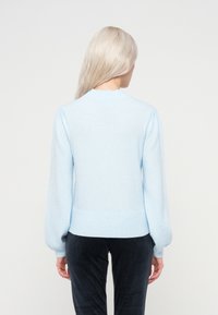 Gaiši zils adīts džemperis ar noapaļotu kakla izgriezumu, pūkainām piedurknēm un ribotu apakšdaļu. Izgatavots no mīksta materiāla, kas paredzēts brīvai pieguvei.